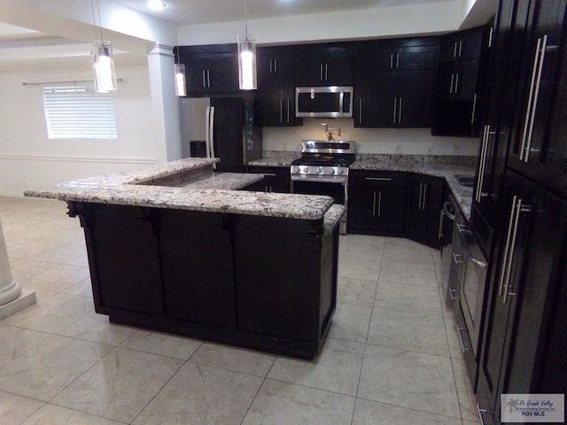 kitchen featuring ornate columns, light stone countertops, stainless steel appliances, pendant lighting, and a center island with sink