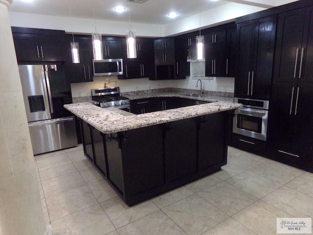 kitchen with sink, light stone countertops, appliances with stainless steel finishes, decorative light fixtures, and a kitchen island