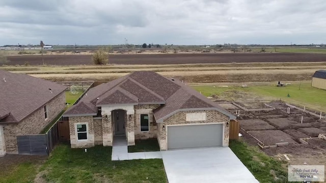 french country inspired facade featuring driveway, an attached garage, a rural view, and brick siding