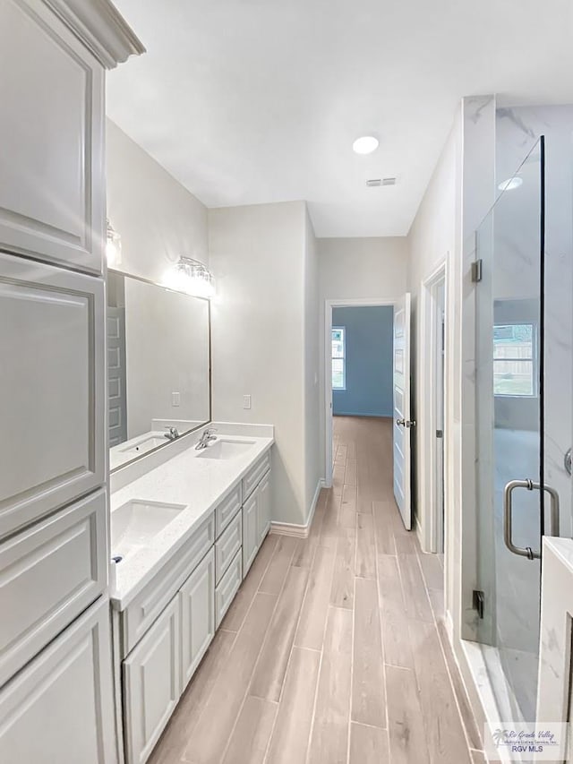 bathroom with a stall shower, double vanity, a sink, and wood finished floors