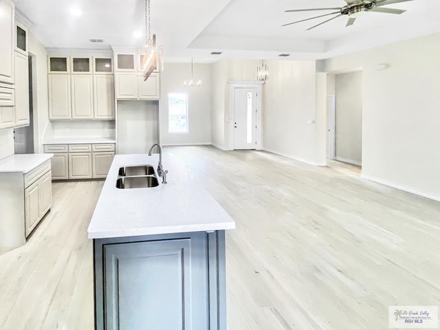 kitchen featuring an island with sink, open floor plan, light countertops, light wood-type flooring, and a sink