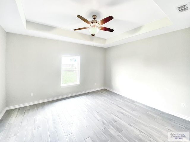 unfurnished room featuring ceiling fan, light wood-style flooring, a raised ceiling, and visible vents