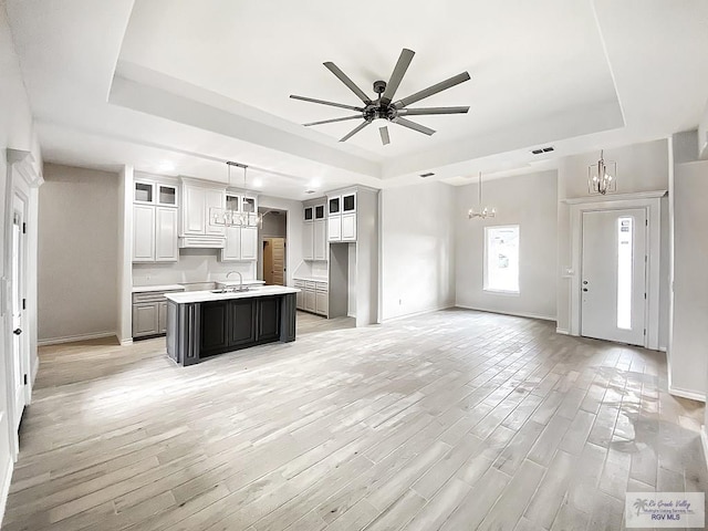 kitchen featuring a tray ceiling, open floor plan, a kitchen island with sink, and light wood finished floors