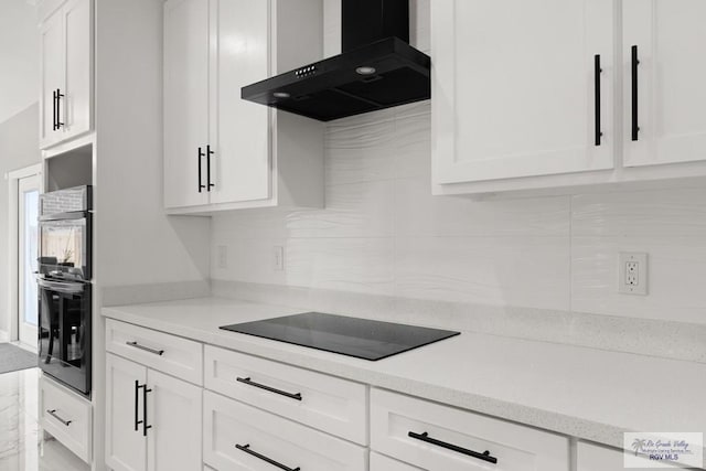 kitchen with black electric stovetop, wall chimney exhaust hood, and white cabinets