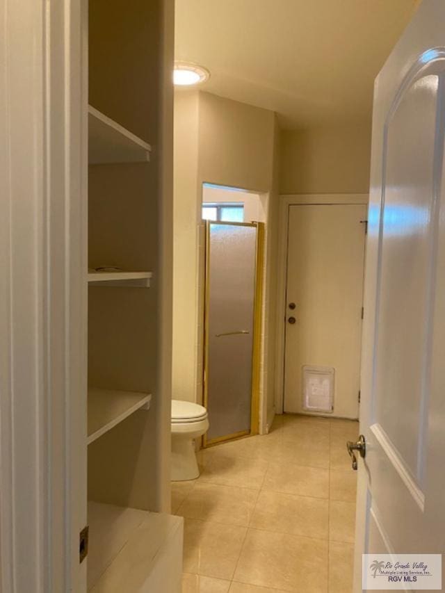 bathroom with tile patterned floors, a shower with door, and toilet