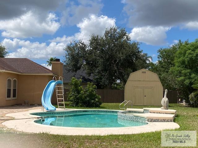 view of pool featuring a yard, a patio, a storage unit, and a water slide