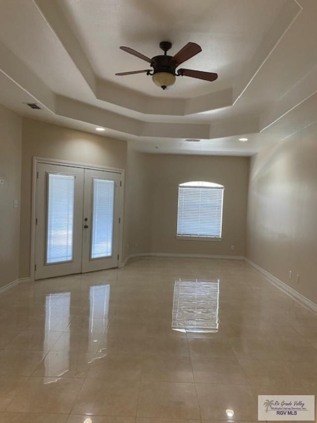 tiled spare room featuring ceiling fan, french doors, and a tray ceiling