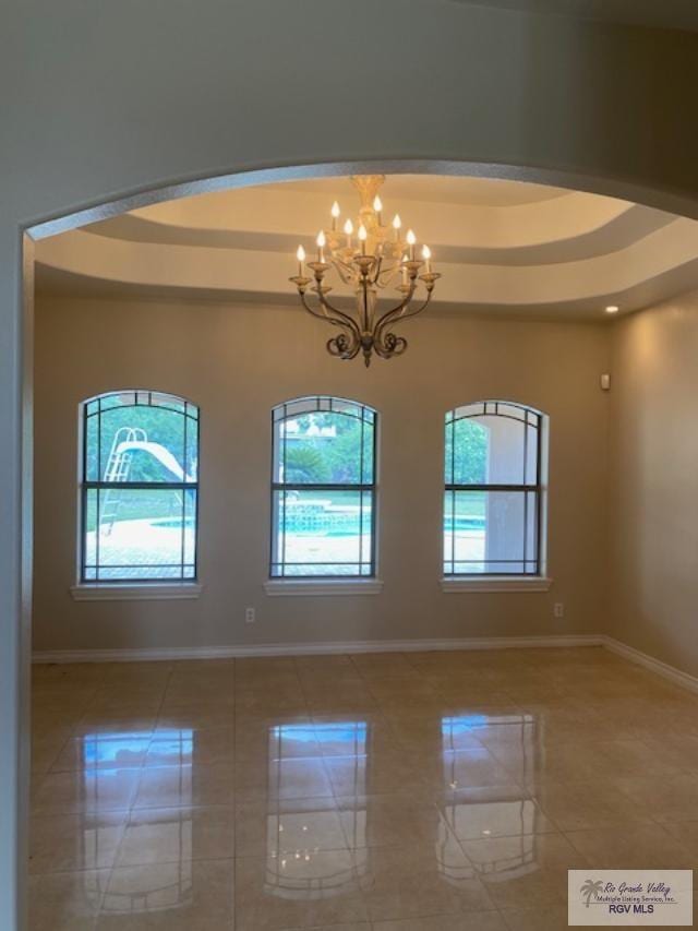 unfurnished room with a raised ceiling, a wealth of natural light, and an inviting chandelier