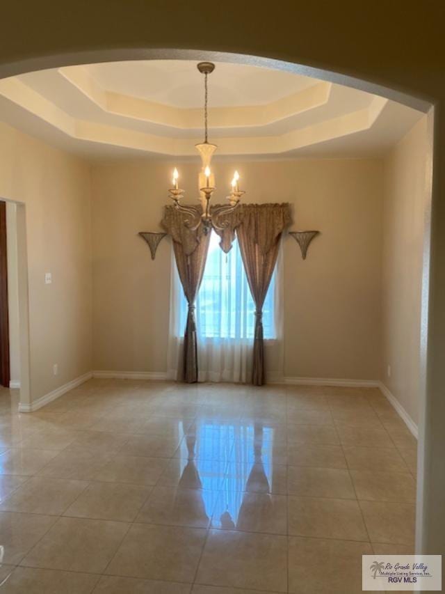 spare room with a tray ceiling, tile patterned flooring, and a chandelier