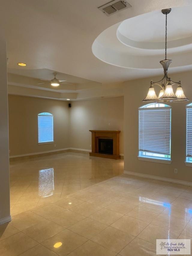 unfurnished living room featuring ceiling fan with notable chandelier, a raised ceiling, and light tile patterned flooring