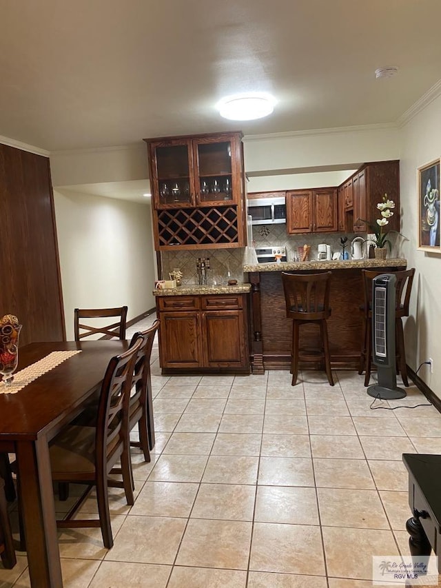 bar featuring light stone countertops, stainless steel appliances, tasteful backsplash, light tile patterned floors, and ornamental molding