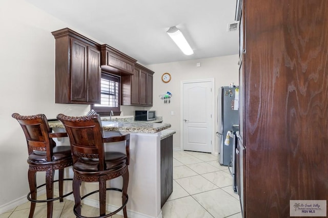 kitchen featuring light stone countertops, stainless steel appliances, kitchen peninsula, a kitchen bar, and light tile patterned floors