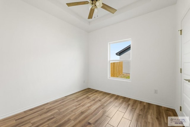 empty room featuring ceiling fan, light hardwood / wood-style floors, and a tray ceiling