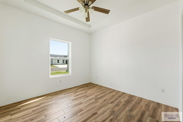 unfurnished room featuring ceiling fan, a raised ceiling, and light wood-type flooring