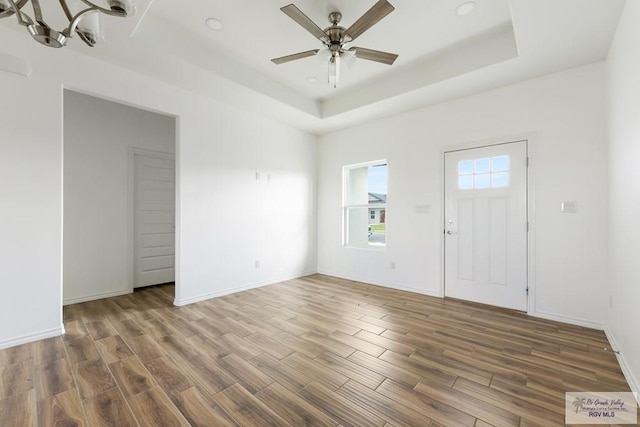 foyer featuring hardwood / wood-style flooring, ceiling fan with notable chandelier, and a raised ceiling