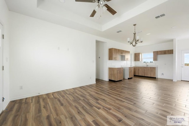 unfurnished living room featuring dark hardwood / wood-style floors, ceiling fan with notable chandelier, and a tray ceiling