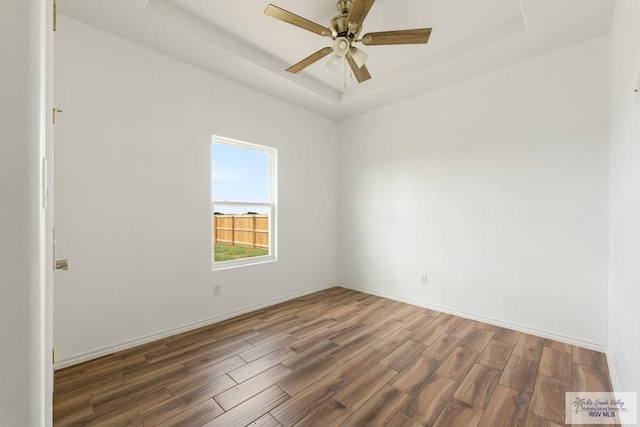 empty room featuring a tray ceiling, ceiling fan, and dark wood-type flooring