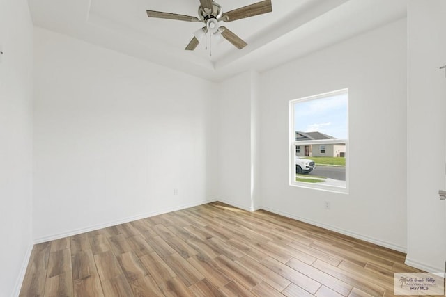 spare room featuring light wood-type flooring, a raised ceiling, and ceiling fan