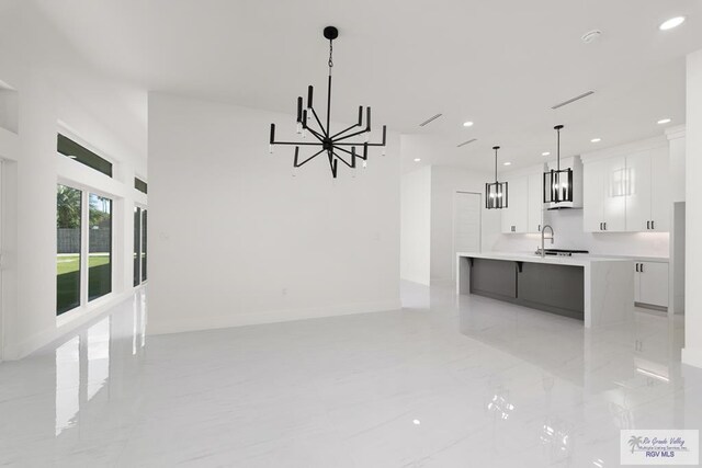 interior space with pendant lighting, a center island, white cabinets, sink, and a notable chandelier