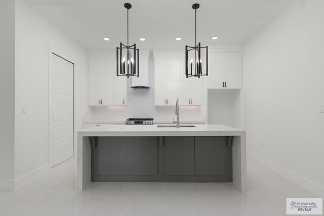 kitchen featuring a large island with sink, white cabinets, sink, wall chimney exhaust hood, and decorative light fixtures