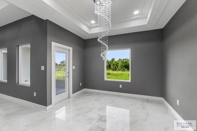 empty room featuring a healthy amount of sunlight, a tray ceiling, and a notable chandelier