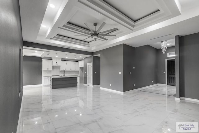 unfurnished living room with ceiling fan with notable chandelier, sink, and a raised ceiling