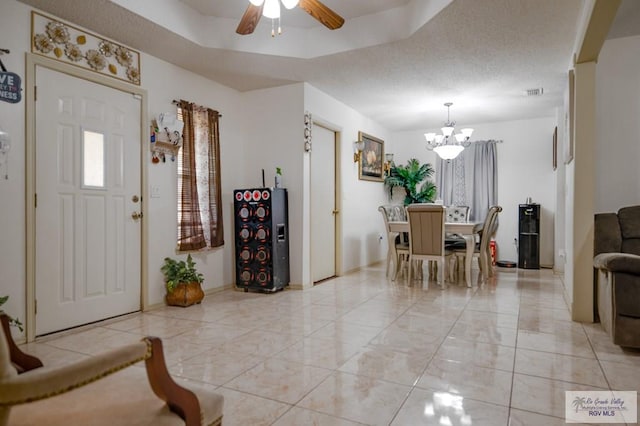 entrance foyer featuring ceiling fan with notable chandelier, a raised ceiling, and a textured ceiling