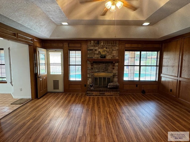 unfurnished living room featuring a textured ceiling, a fireplace, a raised ceiling, and dark wood-type flooring