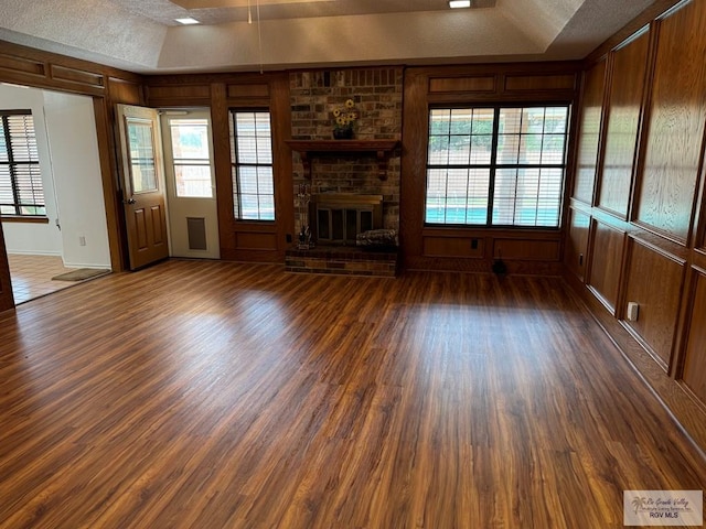 unfurnished living room with a textured ceiling, dark hardwood / wood-style floors, a brick fireplace, and a tray ceiling