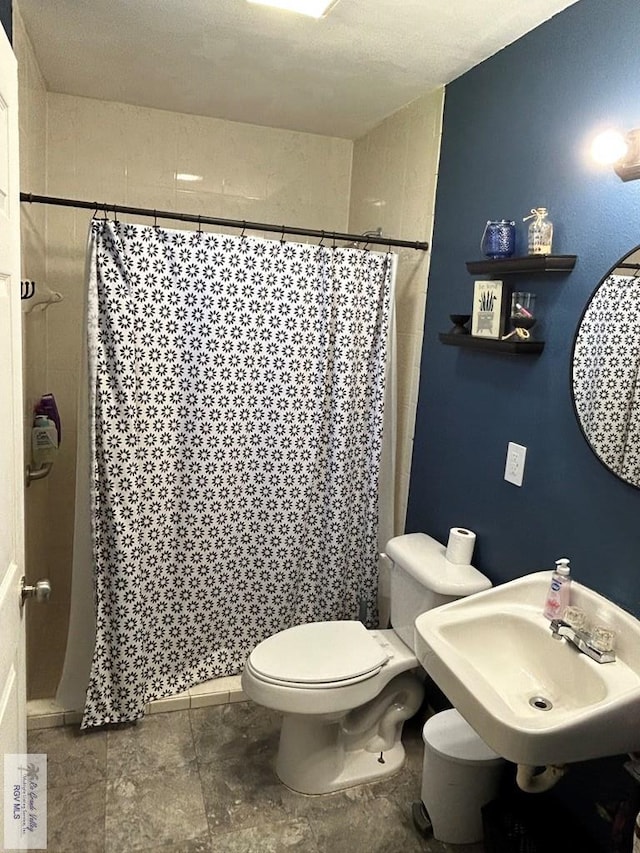 bathroom with a shower with shower curtain, toilet, sink, and a textured ceiling