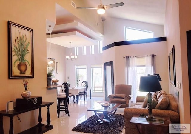 tiled living room with ceiling fan with notable chandelier and a high ceiling