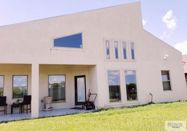 back of property featuring stucco siding, a lawn, and a patio