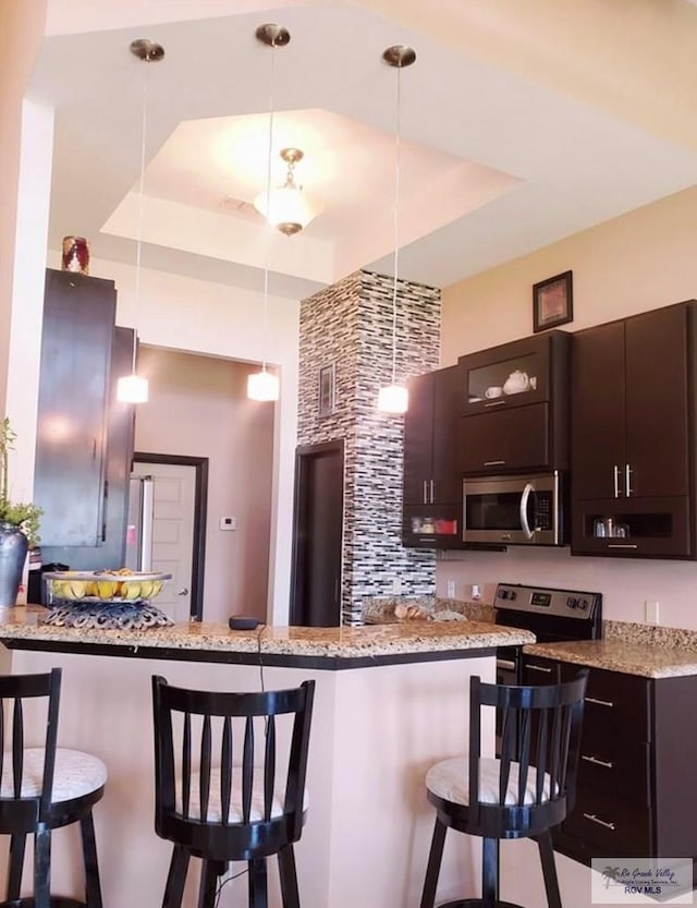 kitchen with a tray ceiling, hanging light fixtures, and appliances with stainless steel finishes