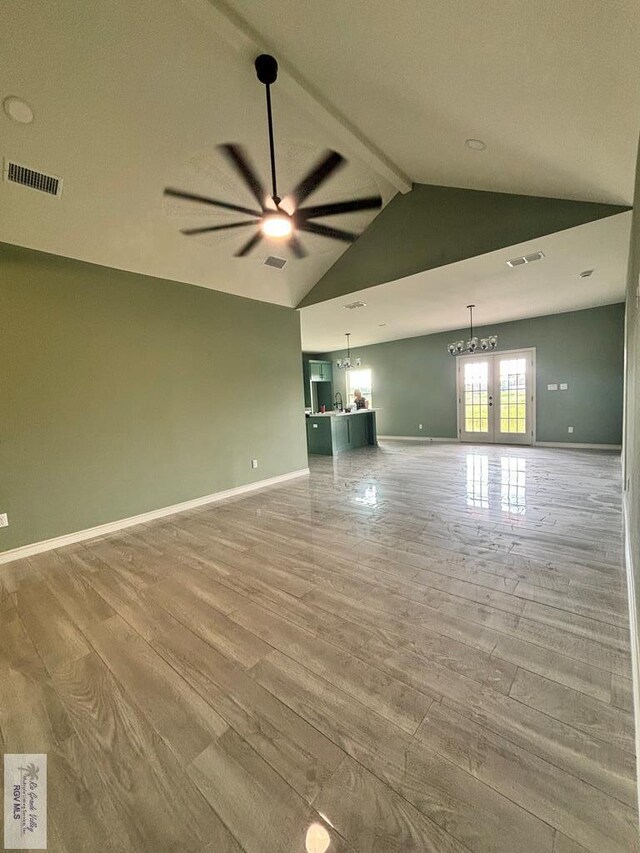 unfurnished living room with hardwood / wood-style floors, vaulted ceiling with beams, ceiling fan, and french doors