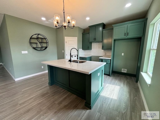 kitchen with sink, a notable chandelier, decorative light fixtures, a kitchen island with sink, and hardwood / wood-style flooring