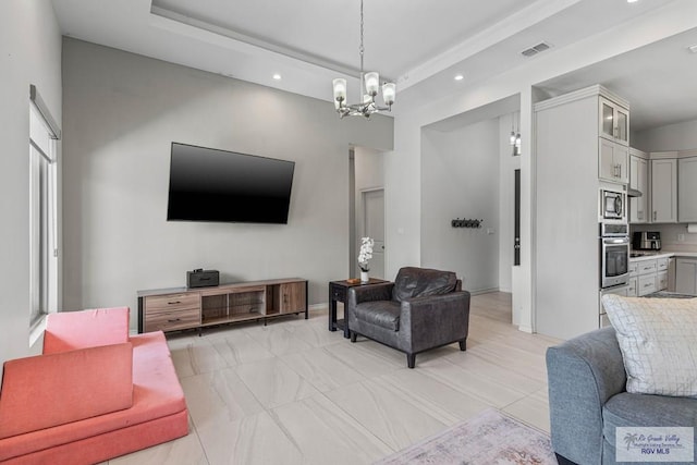 living room featuring visible vents, baseboards, a tray ceiling, recessed lighting, and an inviting chandelier