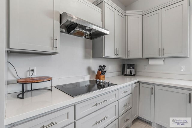 kitchen featuring black electric stovetop, wall chimney exhaust hood, gray cabinets, and light countertops