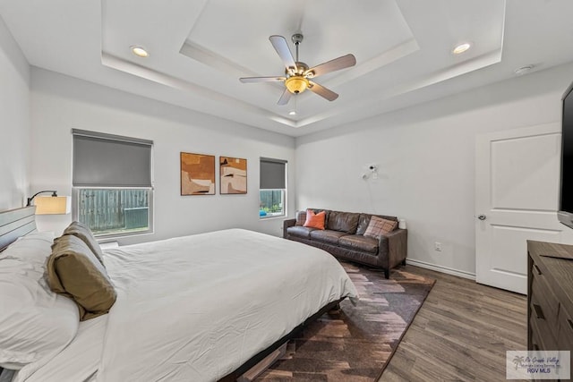 bedroom with recessed lighting, baseboards, a tray ceiling, and wood finished floors