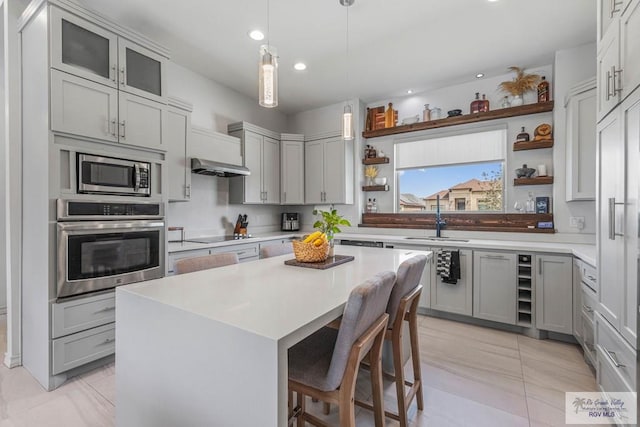 kitchen with appliances with stainless steel finishes, a breakfast bar area, gray cabinetry, and open shelves