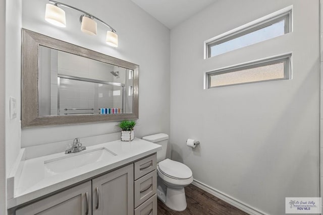 full bath featuring toilet, a stall shower, wood finished floors, baseboards, and vanity