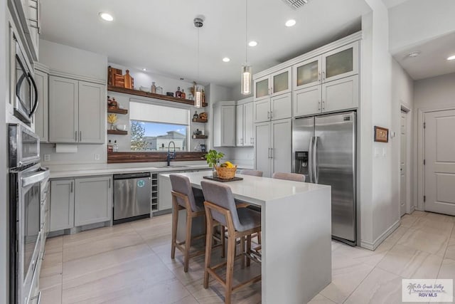 kitchen with open shelves, a sink, light countertops, appliances with stainless steel finishes, and a kitchen breakfast bar