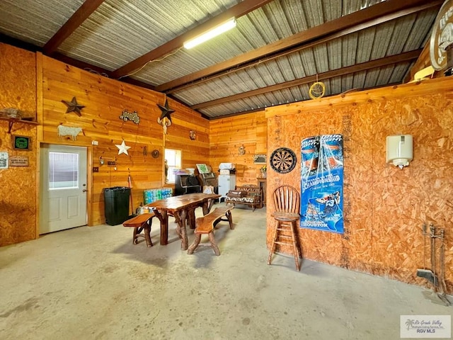 dining room featuring wooden walls, beamed ceiling, and concrete flooring