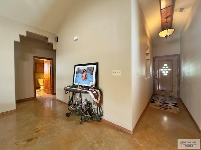 corridor featuring high vaulted ceiling and concrete floors
