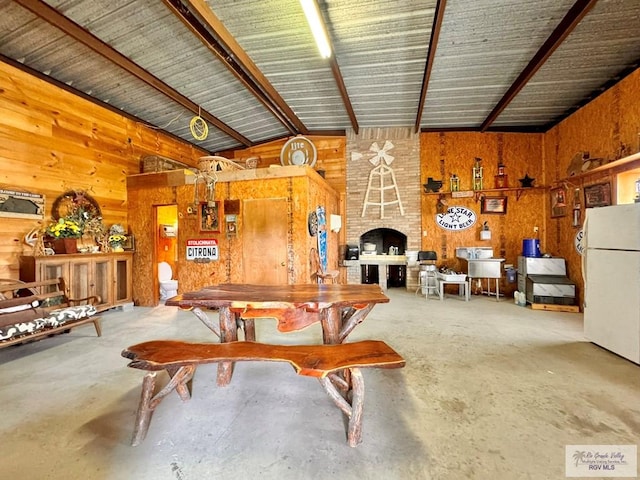 dining room with lofted ceiling with beams, wood walls, concrete flooring, and a fireplace