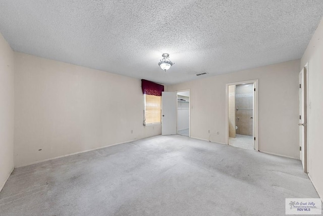 unfurnished bedroom with light colored carpet, a textured ceiling, and ensuite bath