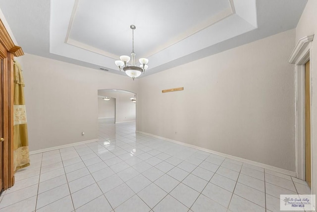 tiled spare room with a raised ceiling and a chandelier