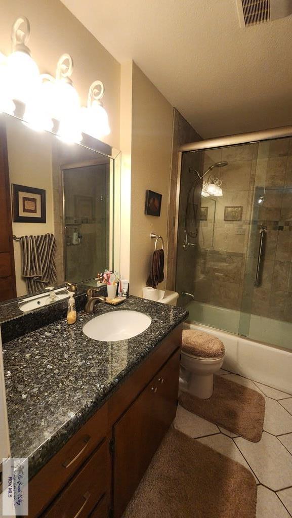 full bathroom with a textured ceiling, vanity, enclosed tub / shower combo, tile patterned flooring, and toilet