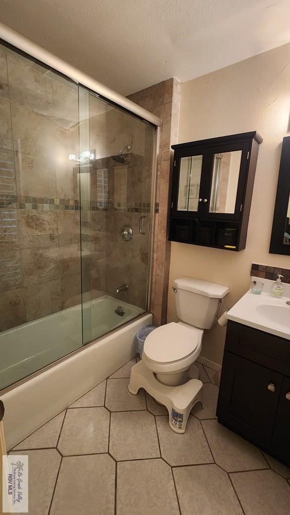 full bathroom featuring tile patterned flooring, a textured ceiling, combined bath / shower with glass door, toilet, and vanity