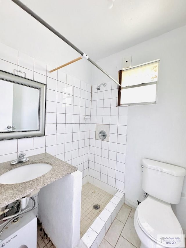 bathroom featuring tile patterned flooring, tiled shower, toilet, and sink