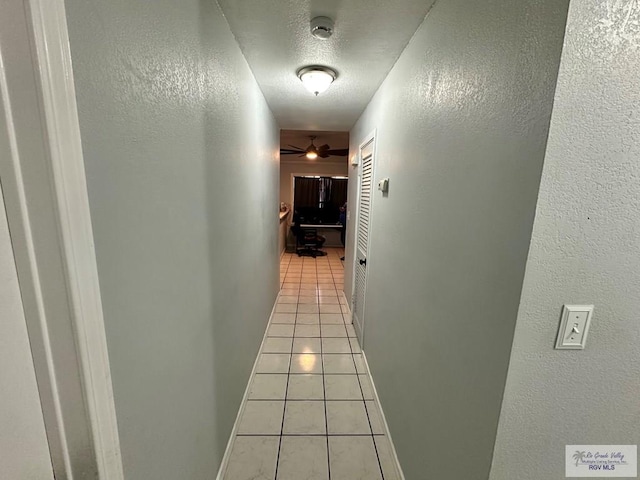 hallway with light tile patterned flooring, a textured ceiling, baseboards, and a textured wall